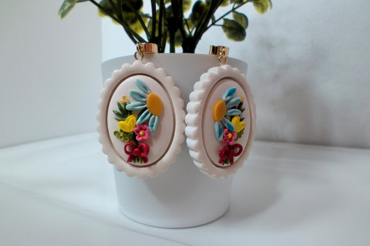 Pair of floral earrings on a white stand with a blurred plant in the background